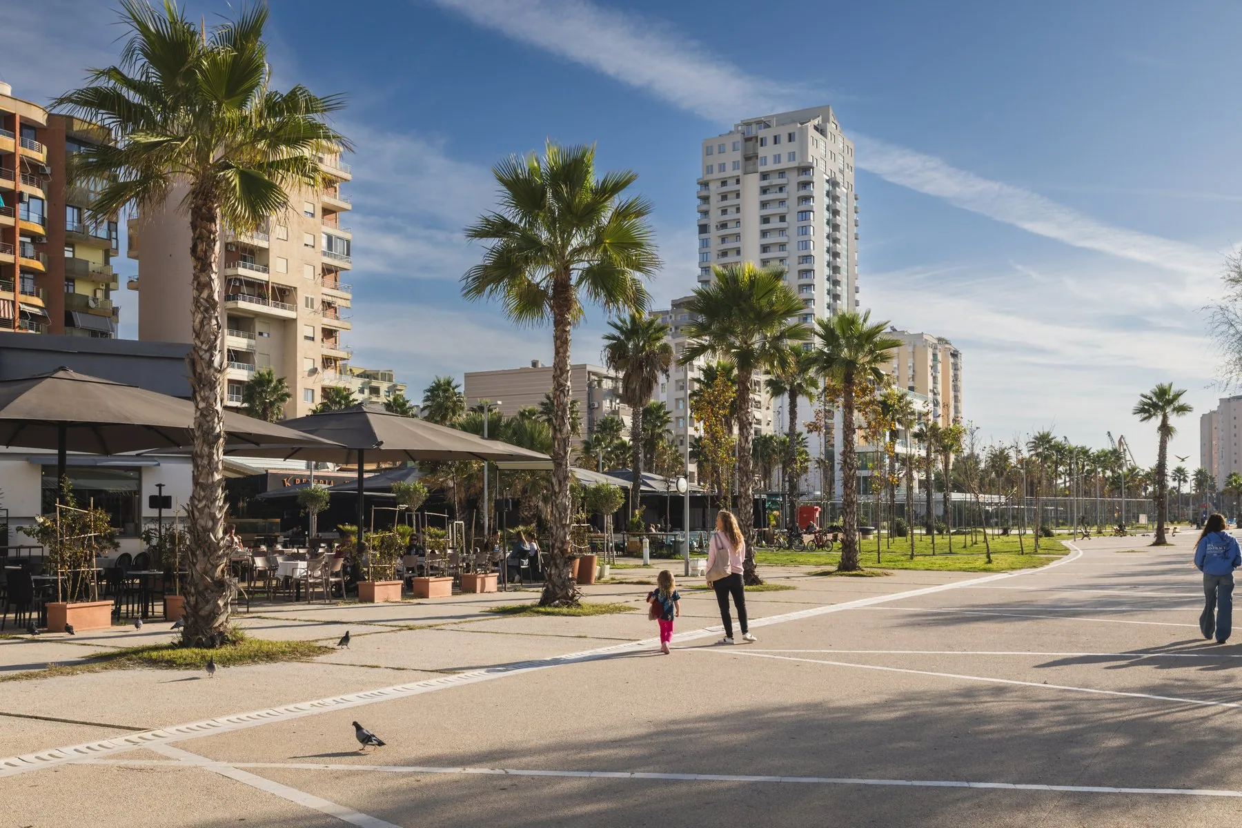 Strandpromenad i Durrës med palmer, uteserveringar och höga bostadshus en solig dag