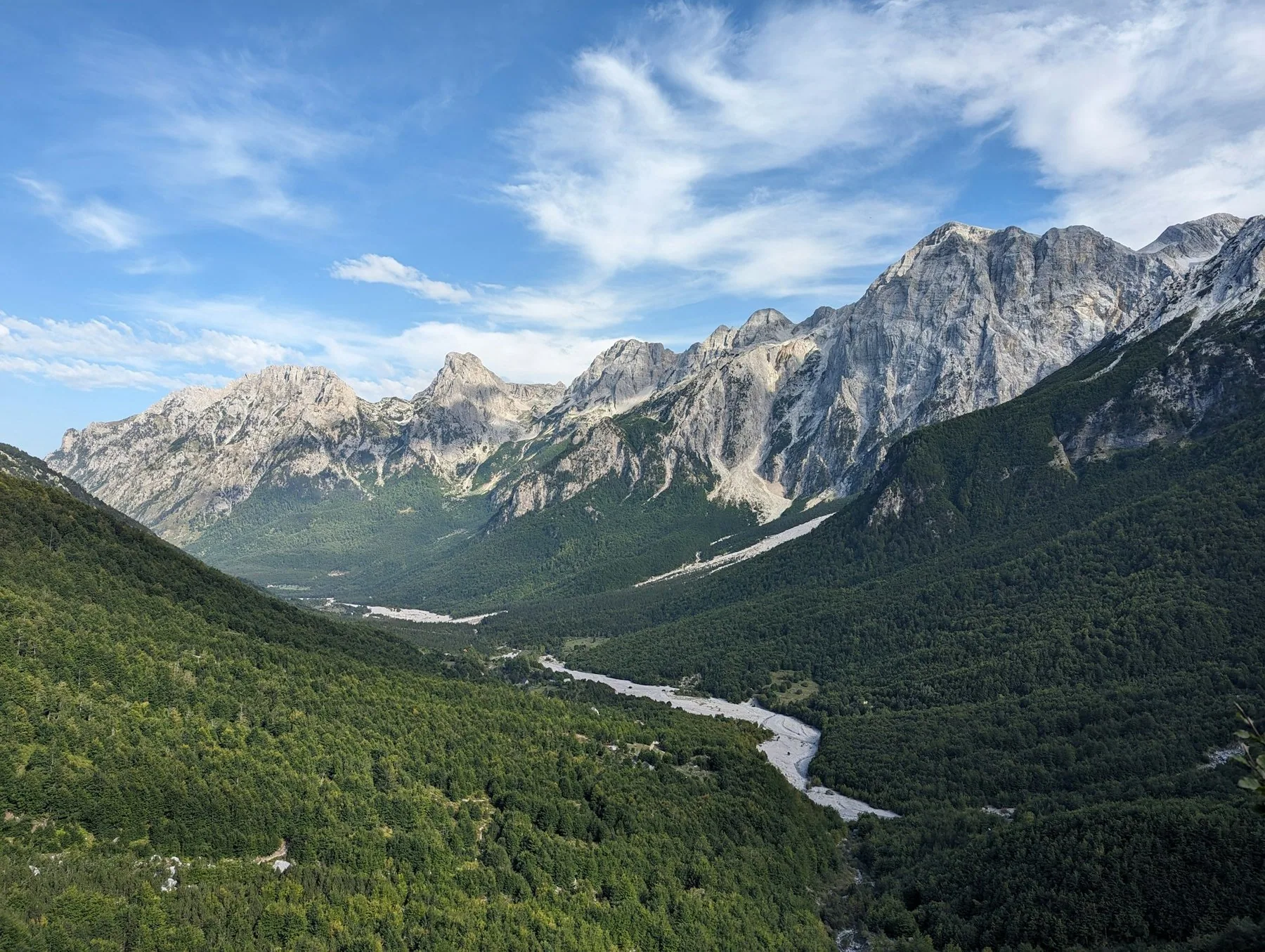 Valbonadalen med skogklädda sluttningar, ett ljust flodfåra i dalbotten och kala kalkstenstoppar