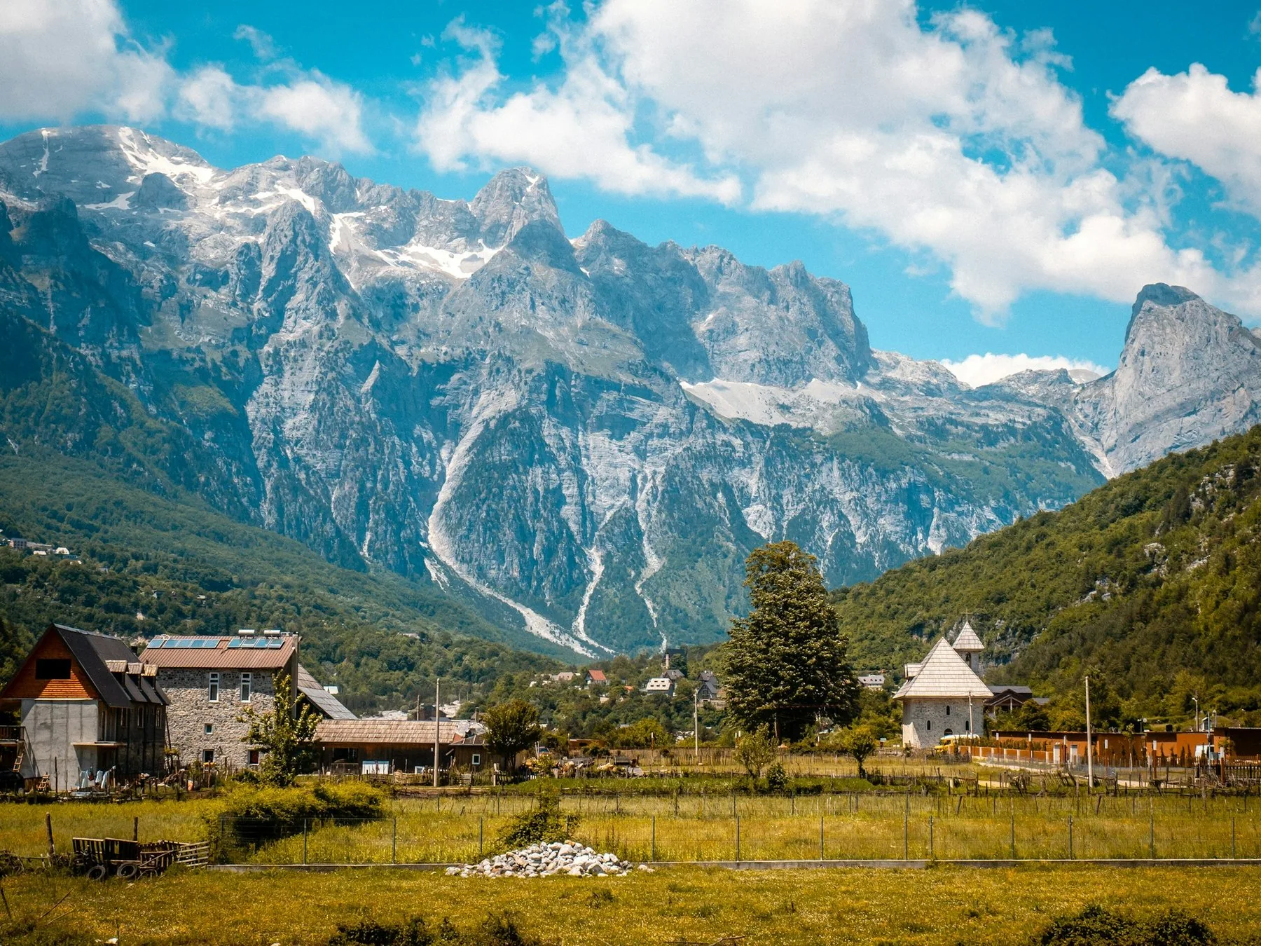 Byn Theth i en grön dal under Albanska alpernas snöfläckiga kalkstenstoppar