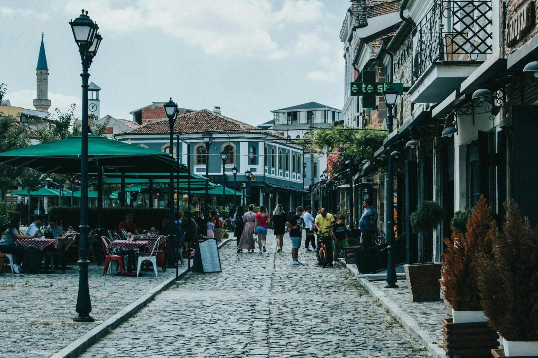 Kullerstensgata i gamla basaren i Korça med uteserveringar, gatlyktor och en minaret i bakgrunden