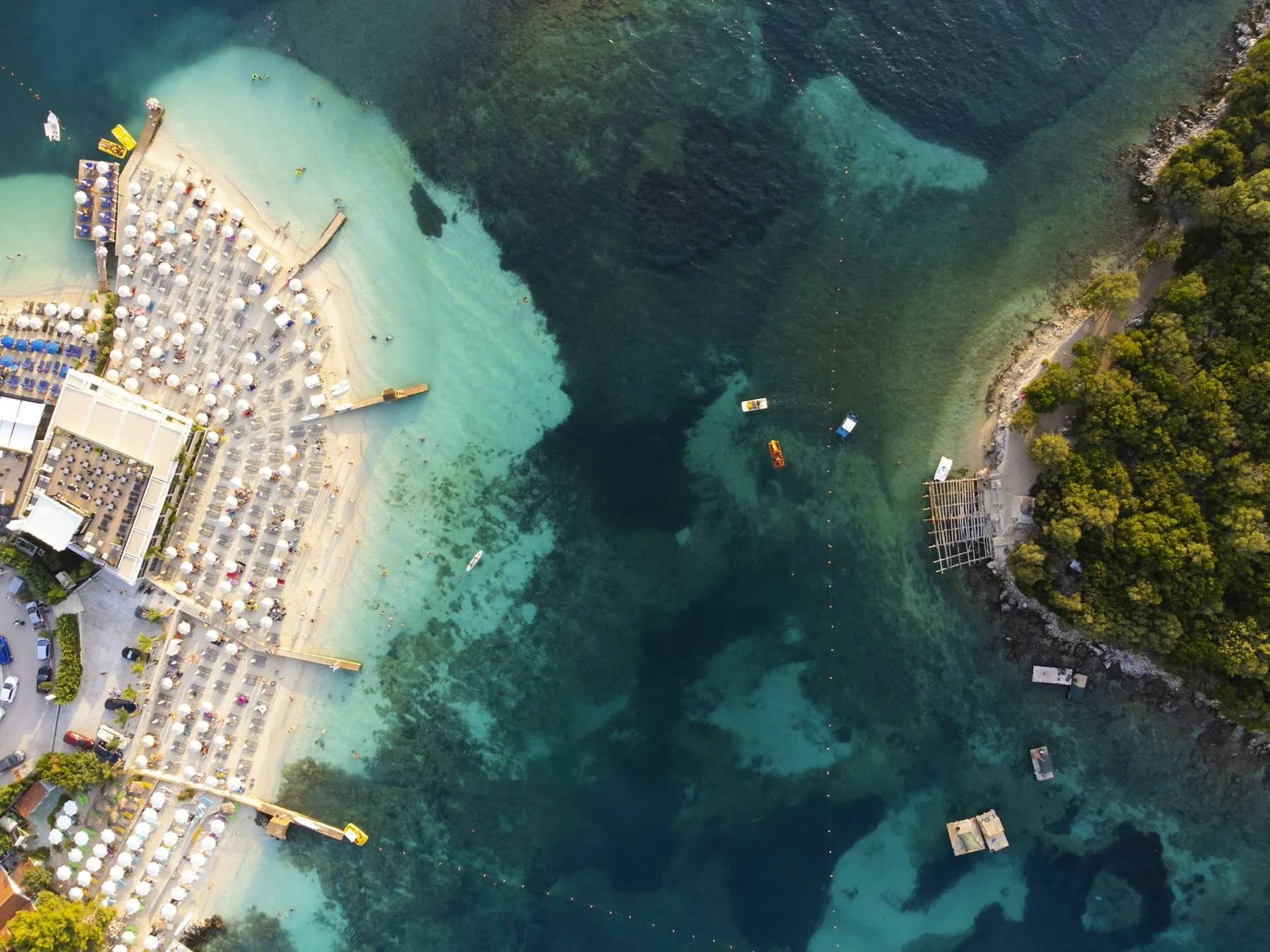 Flygbild över en fullsatt strand med rader av parasoller vid turkost, klart vatten