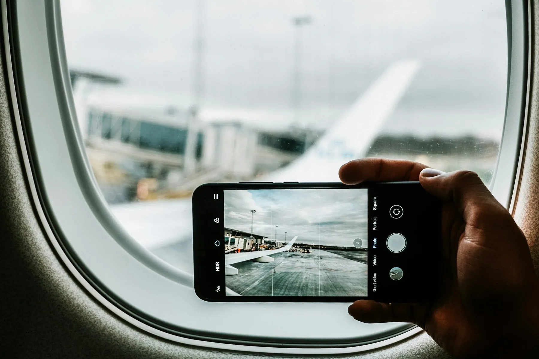 Mobiltelefon fotograferar flygplansvingen genom ett kabinfönster