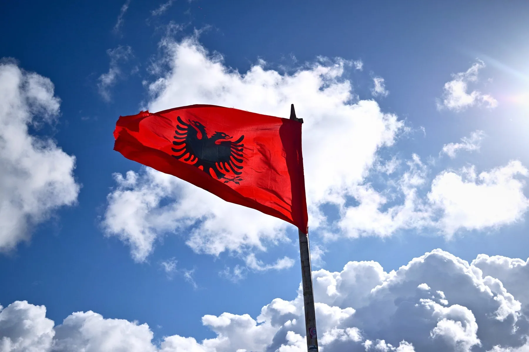 Albanska flaggan med den svarta dubbelörnen fladdrar mot blå himmel och vita moln