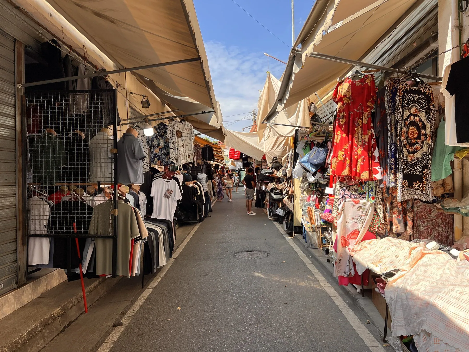 Marknadsstånd med kläder, mattor och textilier längs en gång på Çam-marknaden i Tirana