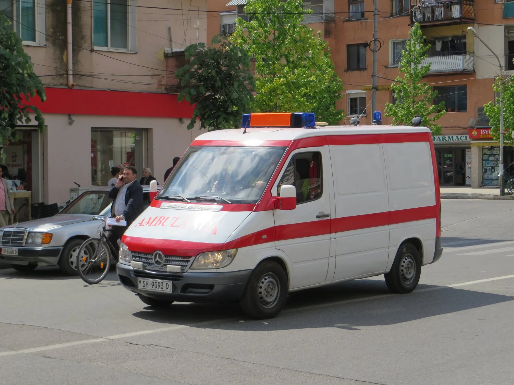 Vit och röd ambulans med blåljus på en gata i en albansk stad