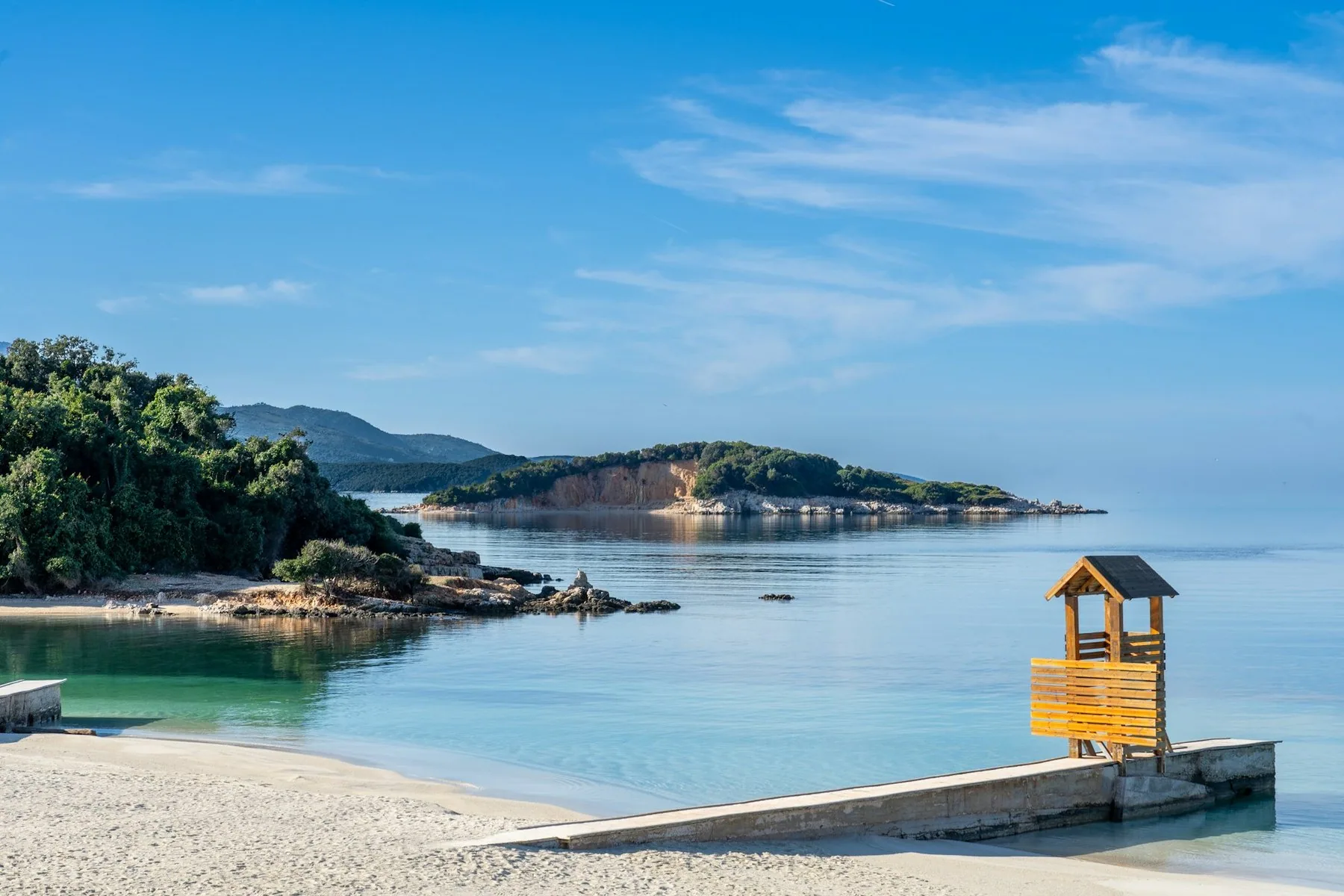 Stilla vik med små öar och ett trätorn för strandvakten på en sandstrand i Ksamil