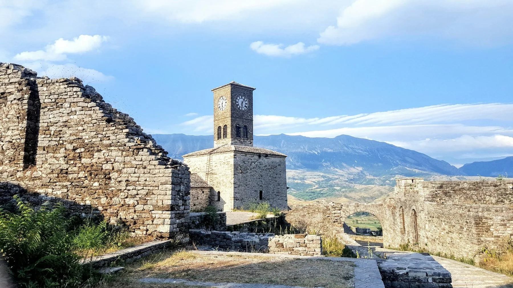Klocktornet och stenmurarna i Gjirokastras borg mot blå himmel och bergen i Drinodalen